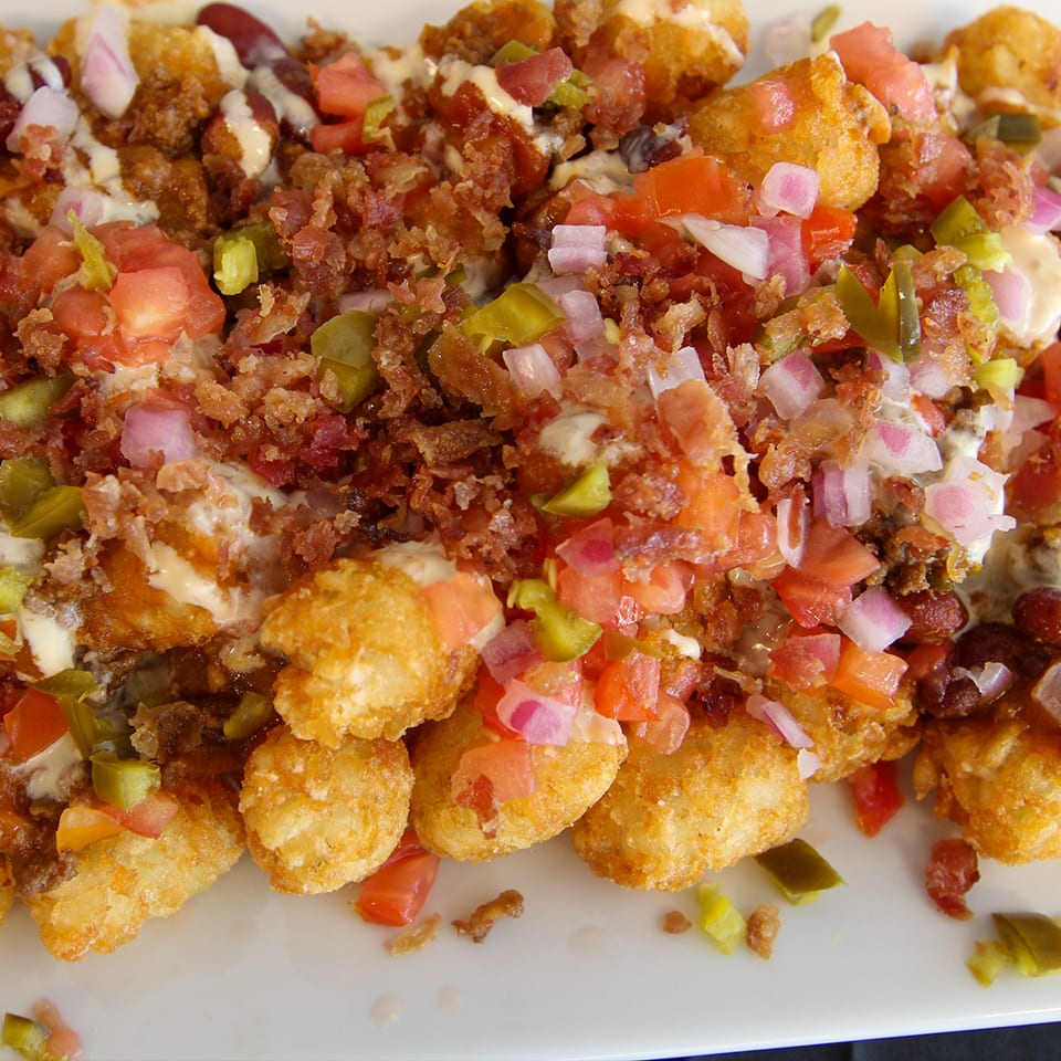 Loaded plate of golden fried bites topped with bacon, diced tomatoes, onions, jalapeños, and creamy sauce.