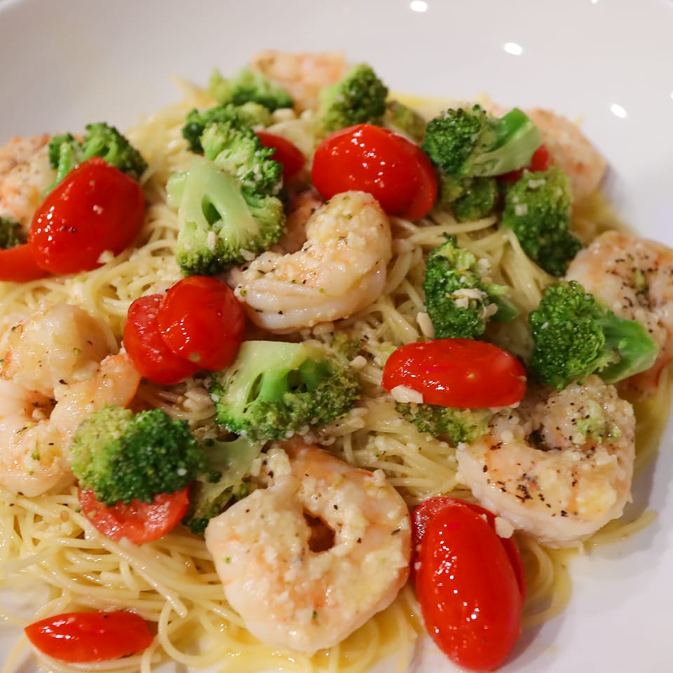 Plate of angel hair pasta topped with shrimp, broccoli florets, and glossy cherry tomatoes.