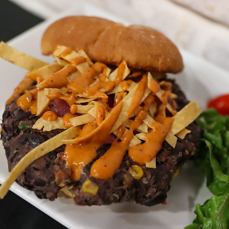Black bean burger topped with tortilla strips and orange sauce, served with lettuce.