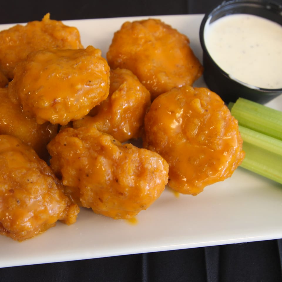 Buffalo-style chicken bites served with celery sticks and creamy dipping sauce on a white plate.